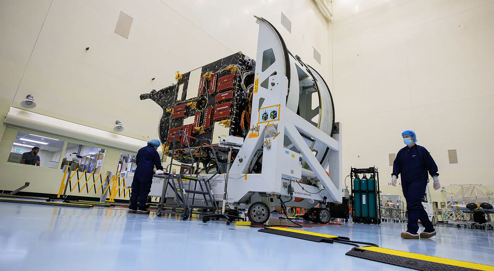 The Psyche spacecraft in a clean room, gold foil and instruments open under the lights.