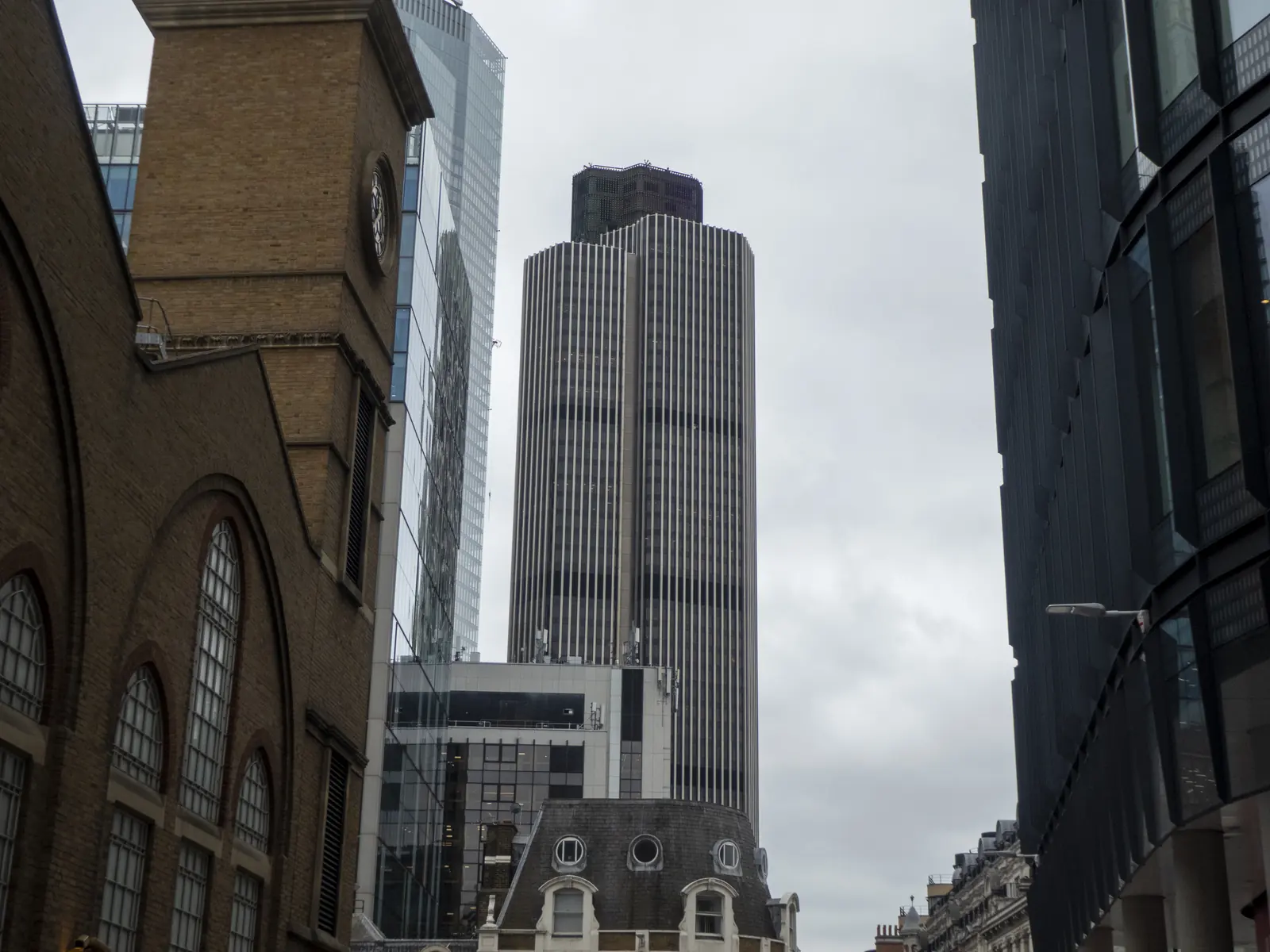 Tower 42 rising above the City of London, its dark glass and steel shaft seen from Old Broad Street.