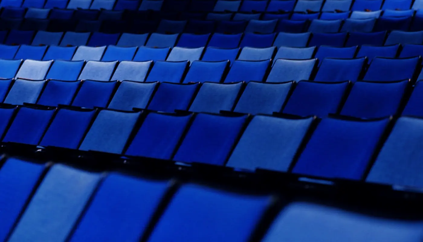 Empty blue seats filling an auditorium, house lights up, no one in the frame.