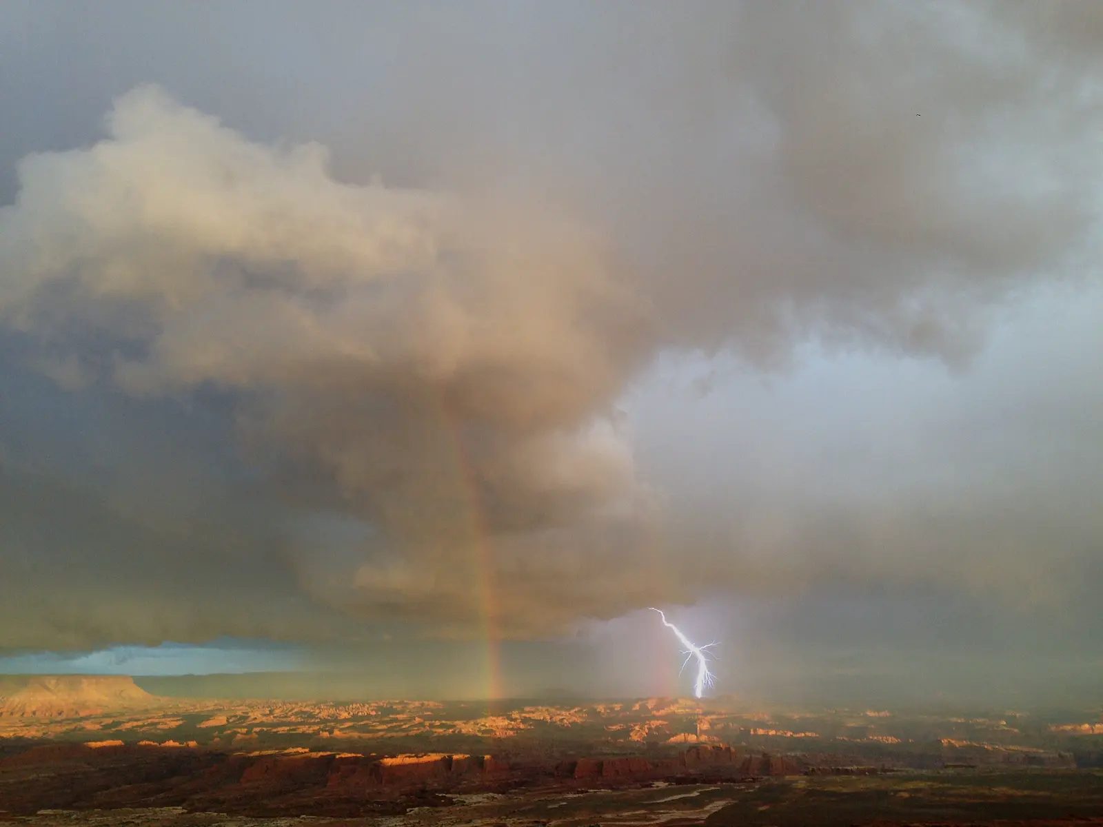 Lightning and a rainbow over Canyonlands, storm light on a dark sky.