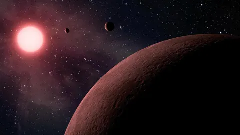 Artist’s picture of a small red star with three rocky planets packed close, like a miniature Jupiter family.