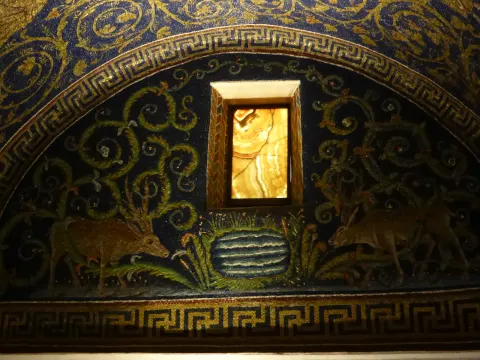 Fifth-century mosaic lunette in the Mausoleum of Galla Placidia, Ravenna: two deer approach a pool of water among gold vine scrolls on a deep blue ground.